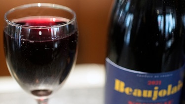 Wein auf Bier - das rat´ ich dir! Stimmt das? Auf dem Bild steht ein eingeschenktes Glas Beaujolais neben einer vollen Flasche.  | Bild: dpa-Bildfunk