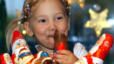 Ein Mädchen isst einen Schokoladen-Nikolaus. | Bild: picture-alliance / dpa | Achim Scheidemann