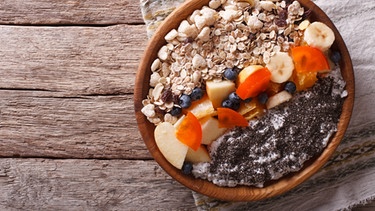Auf einem Holzboden sieht man eine zubereitete Frühstücksbowl mit Chiasamen, Granola und Obst. Welche Superfoods sind wirklich super? Und was ist eher Unsinn? | Bild: Colourbox.com