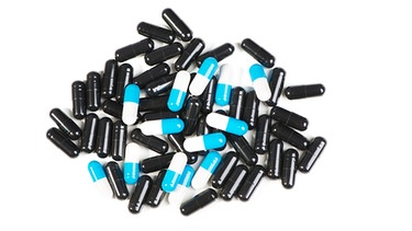 Weißer Untergrund, darauf verteilt viele schwarzen Pillen mit wenigen blau-weißen dazwischen. Vitaminpillen versprechen manchmal das Blaue vom Himmel. Die wissenschaftliche Studienlage hingegen zeichnet ein ganz anderes Bild. | Bild: Colourbox.com