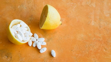 Oranger Hintergrund, darauf eine halbierte Zitrone: Eine Hälfte ist normal, die andere ausgehöhlt und mit weißen Tabletten gefüllt. Mittlerweile gibt es so viele Vitamine in Pillen-, Tabletten- oder Pulverform. Braucht man die? Bringen die was? Und wie schaut es mit anderen Vitaminen aus? | Bild: Colourbox.com