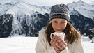 Junge Frau trinkt Kakao vor winterlicher Bergkulisse. | Bild: picture-alliance / Image Source | Image Source/Kalle Singer
