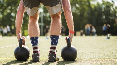 Mann hebt Kettle-Bell Gewichte an, um bei CrossFit Wettbewerb teilzunehmen. Extreme Belastung kann dazu führen, dass sich Muskeln auflösen, ein Syndrom, das Rhabdomyolyse genannt wird. | Bild: picture-alliance/dpa