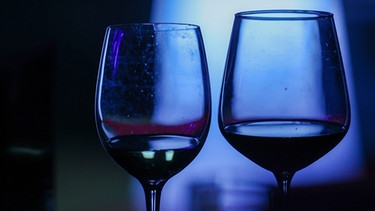 Zwei Gläser mit Rotwein schimmern im blauen Licht. | Bild: picture alliance / PHOTOPQR/L'EST REPUBLICAIN/MAXPP | Lionel VADAM