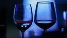 Zwei Gläser mit Rotwein schimmern im blauen Licht. | Bild: picture alliance / PHOTOPQR/L'EST REPUBLICAIN/MAXPP | Lionel VADAM