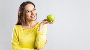 Eine Frau hält einen Apfel in der Hand. Das Immunsystem ist ein Schutzschild, das den Körper vor Krankheitserregern schützt. Ausreichend Schlaf und eine vitaminreiche Ernährung helfen die Körperabwehr zu stärken.  | Bild: Colourbox