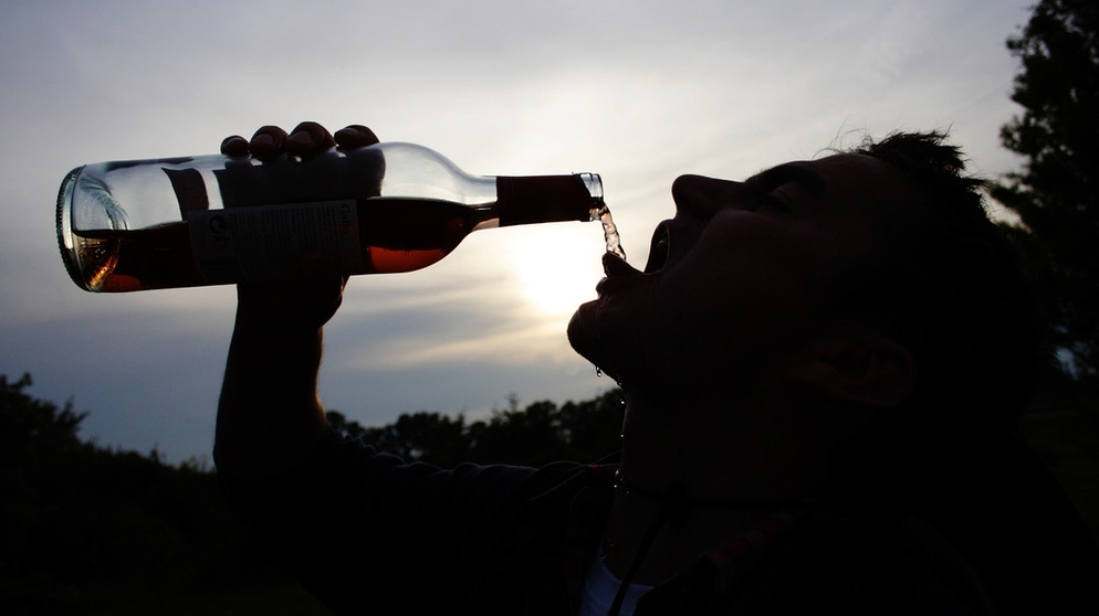 Alkohol - schon über die Schleimhäute im Mund gelangt er in unseren Körper. Im Bild: Ein silhouettenhaft dargestellter Mann trinkt aus einer Weinflasche.  | Bild: picture-alliance/dpa/dpa-Zentralbild/Daniel Gammert
