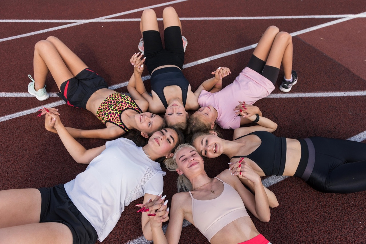 Sechs junge Frauen liegen glücklich und ausgepowert auf dem Boden eines Sportstadions. Sie halten sich an den Händen und liegen mit ihren Köpfen aneinander wie ein Stern. | Bild: picture alliance / Zoonar | Ruslan Olinchuk