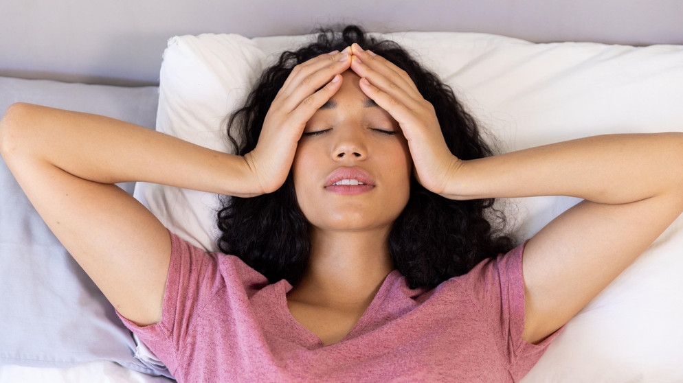Wetterfühlige Frau hat Migräne Kopfschmerz. Sie hält sich die Hände an die Schläfen und liegt auf einem Bett. | Bild: picture alliance / Zoonar | Channel Partners