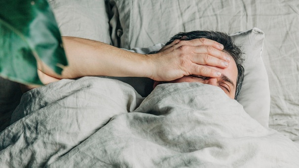 Eine Mann liegt erschöpft im Bett. Die Krankheit Myalgische Enzephalomyalgie oder ME/CFS ist auch bekannt als Chronisches Erschöpfungssyndrom. Sie fühlt sich an wie eine jahrelang andauernde Grippe. | Bild: picture alliance / Westend61 | Vira Simon