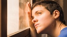 Frau sieht deprimiert aus dem Fenster. Die Krankheit Myalgische Enzephalomyalgie oder ME/CFS ist auch bekannt als Chronisches Erschöpfungssyndrom. Sie fühlt sich an wie eine jahrelang andauernde Grippe. | Bild: picture alliance / Westend61 | Mar