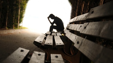 Eine depressive Person sitzt auf einer Parkbank. | Bild: stock.adobe.com/hikrcn
