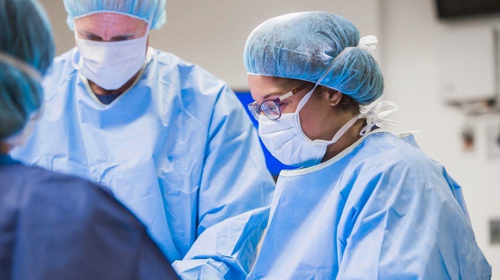 Eine Chirurgin mit ihren Kollegen im OP-Saal | Bild: picture alliance/Bildagentur-online/Blend Images | Blend Images/John Fedele
