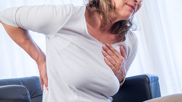 Eine Frau fasst sich im Schmerz an Brust und Rücken.  | Bild: picture alliance/dpa Themendienst | Christin Klose
