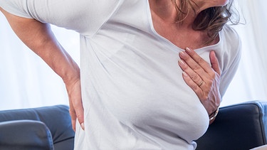 Eine Frau fasst sich im Schmerz an Brust und Rücken.  | Bild: picture alliance/dpa Themendienst | Christin Klose