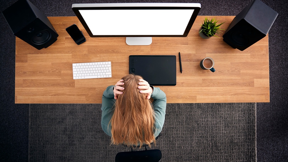 Stress kann Migräne auslösen. Im Bild Frau am Schreibtisch mit Computer hält sich den Kopf. | Bild: picture alliance / Shotshop | Monkey Business 2