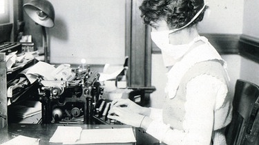 Epidemien vor Corona: Schreibkraft im Medizinbetrieb mit Schutzmaske während der Epidemie 1918 in den USA. | Bild: picture-alliance/dpa