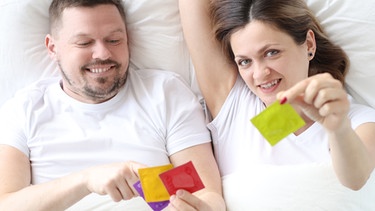 Paar liegt auf dem Bett mit Kondomen in der Hand. Hält Slow Sex fit und verändert sich Sex im Alter? | Bild: colourbox.com