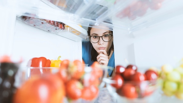 Eine Frau schaut in einen Kühlschrank, in dem diverse Lebensmittel liegen. | Bild: colourbox.com