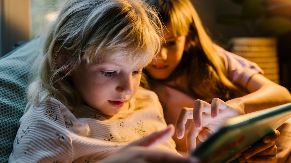 Zwei Mädchen lesen mit einem Tablet in der Hand. Gut lesen zu können, ist wichtig für das erfolgreiche Lernen. Wie ihr Kinder beim Lesenlernen unterstützen könnt und warum Vorlesen eine besondere Rolle spielt. | Bild: picture alliance/Westend61/Tanya Yatsenko