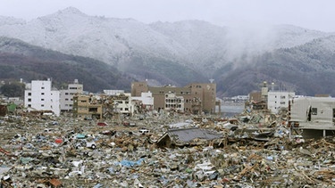 Onagawa in der Präfektur Miyagi im Nordosten Japans ist nach dem schweren Erdbeben und Tsunami vom 11. März 2011 ein einziges Trümmerfeld, im Hintergrund die schneebedeckten Berge. | Bild: picture alliance / dpa | Kyodo