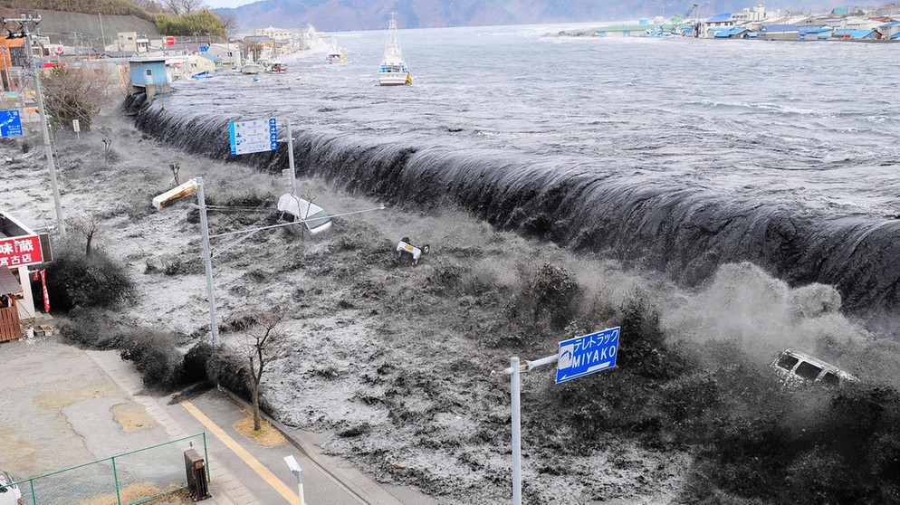 Hier bricht bei der Mündung des Flusses Hei die Tsunamiwelle herein, nach dem schweren Erdbeben im Nordosten Japans am 11. März 2011. Starke seismische Aktivitäten und Verschiebungen tektonischer Platten können riesige Flutwellen, japanisch: Tsunamis auslösen. | Bild: picture-alliance/dpa