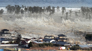 Nach dem schweren Erdbeben am 11. März 2011 bricht eine gigantische Tsunami-Welle über den Nordosten Japans herein, hier in Natori in der Präfektur Miyagi. DIe Folge des Tsunamis war die Atomkatastrophe in Fukushima. | Bild: picture alliance / dpa | Aflo/mainichi Newspaper
