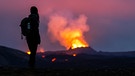 Lava tritt aus dem Krater eines Vulkans in der Nähe des Berges Litli-Hrútur aus, etwa 40 Kilometer südwestlich von Reykjavik. Im Vordergrund steht eine junge Frau und blickt auf die Flammen.  | Bild: picture alliance/dpa | Philipp Schulze