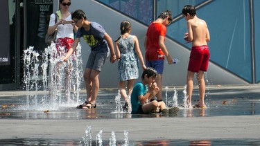 Menschen kühlen sich im Sommer an einem Springbrunnen ab. | Bild: dpa/NurPhoto