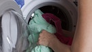 Frau füllt Wäsche in eine Waschmaschine. | Bild: picture alliance / dpa Themendienst