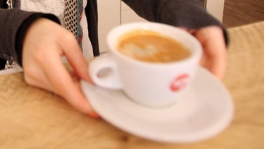 Frau nimmt eine Tasse Kaffee von der Theke | Bild: picture-alliance/dpa