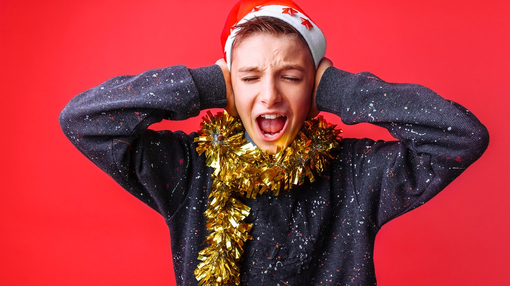 Wie wird man einen Ohrwurm wieder los? Teenager mit Nikolaus-Mütze hält sich die Ohren zu. Hier erfahrt ihr spannende und kuriose Fakten über Weihnachten: Welches ist der beliebteste Weihnachtsbaum, wo stand der größte Christbaum der Welt - und was ist eine Weihnachtsgurke?  | Bild: colourbox.com