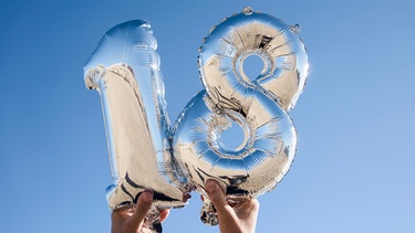 Symbolbild: zwei Hände halten zwei silberne Luftballons in Form einer achtzehn in den Himmel. | Bild: colourbox.com