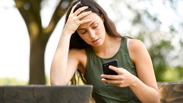 Eine junge Frau im Park schaut verzweifelt auf ihr Smartphone | Bild: picture alliance / dpa Themendienst | Tobias Hase