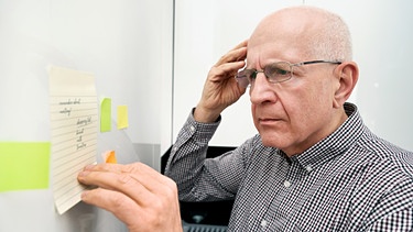Ein älterer Mann schaut zerstreut auf eine Notiz. Wann wird aus Vergesslichkeit Demenz? Frontotemporale Demenz und Alzheimer gibt es manchmal auch bei jungen Menschen. Auch Bruce Willis ist daran erkrankt. Was sind frühe Symptome und Ursachen? | Bild: colourbox.com