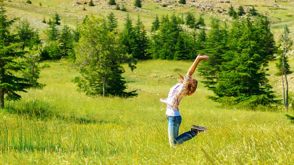 Junge Frau springt glücklich auf einer Wiese in die Luft. Was ist Glück? Wann fühlt man es und wie? Und kann man dem Glücksgefühl auch auf die Sprünge helfen? Wir haben für euch Infos und Tipps zum Glücklichsein gesammelt. | Bild: colourbox.com