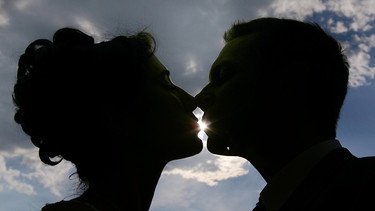 Ein Kuss im Gegenlicht: Paar, das sich küsst. Die berühmtesten Filmküsse, Kuss-Traditionen in anderen Ländern und Reaktionen des Körpers während des Knutschens - hier erfahrt ihr alles Wichtige rund um den Kuss. | Bild: picture-alliance/dpa