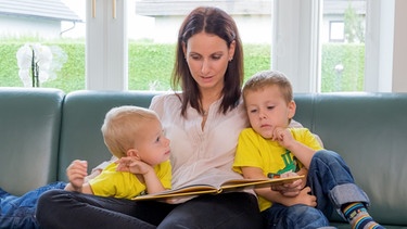 Eine Mutter liest Ihren Kindern ein Märchen aus einem Buch vor. | Bild: stock.adobe.com/Gina Sanders