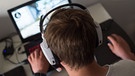 Ein Mann sitzt mit einem Headset vor einem Laptop und spielt ein Online-Computerspiel. | Bild: dpa-Bildfunk/Lino Mirgeler