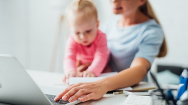 Frau sitzt mit Baby und Telefon vor Laptop. Multitasking kann zum Burnout führen.  | Bild: colourbox.com