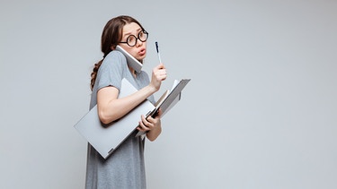 Frau mit Brille spricht am Handy und hat einen Laptop und Zettel in der Hand. Hier erfahrt ihr, welche Formen von Perfektionismus es gibt, wann er krankhaft ist und wann er nützt.  | Bild: colourbox.com