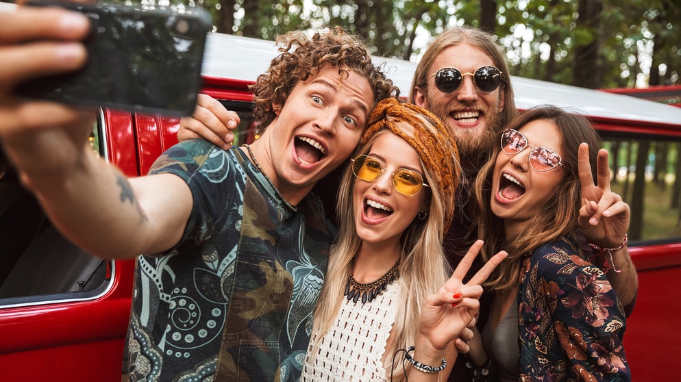 Junge Menschen im Hippie-Look machen ein Selfie vor einem VW-Bus. Positiv denken und optimistisch bleiben: Laut der Positiven Psychologie können wir Optimismus lernen. Wann sind Tipps für mehr Zuversicht wirklich hilfreich und wann wird positives Denken toxisch? | Bild: colourbox.com