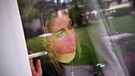Frau mit Maske blickt aus dem Fenster.  | Bild: picture-alliance/dpa