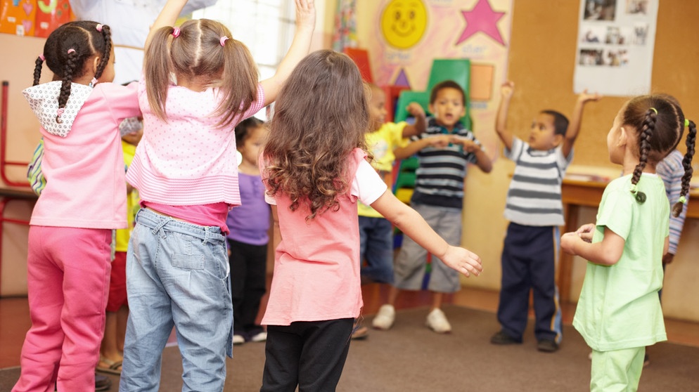 Kindergartenkinder bilden stehend einen Morgenkreis. Ab einem bestimmten Alter ist der Umgang mit Gleichaltrigen enorm wichtig für das Erlernen von Sozialkompetenz.  | Bild: colourbox.com