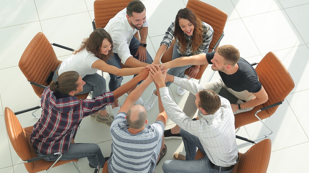 Sieben Männer und Frauen sitzen im Kreis auf Stühlen und reichen sich die Hände. Teamfähigkeit ist eine der wichtigsten Eigenschaften, die Arbeitgeber an ihren Mitarbeitern schätzen. | Bild: colourbox.de