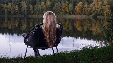 Junge Frau sitzt in einem Stuhl und blickt auf einen See. Einsamkeit kann jeden treffen und ist in Deutschland weit verbreitet, besonders Jugendliche und junge Erwachsene sind betroffen. Warum Einsamkeit krankmachen kann und welche Strategien euch helfen, sie zu überwinden. | Bild: picture alliance/Caro Sorge
