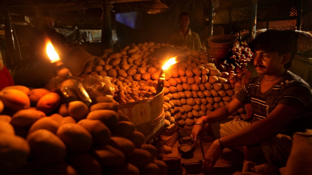 Indien, 2012: Ein indischer Gemüsehändler wartet während eines massiven Stromausfalls auf einem lokalen Markt in Kalkutta, Indien, am 31. Juli 2012 auf Kunden. Hunderte von Millionen Indern hatten in mehr als der Hälfte des Landes kein Strom. | Bild: picture alliance / dpa | Piyal Adhikary