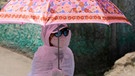 Hitzewelle in Indien und Pakistan im April 2022: Eine junge Frau schützt sich mit einem Regenschirm und einem Schal vor der Hitzewelle im Staat Uttar Pradesh in Indien.  | Bild: picture alliance / ASSOCIATED PRESS | Rajesh Kumar Singh