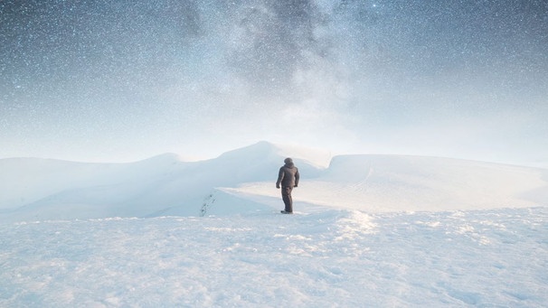 Ein Mann von hinten steht vor einer Schneelandschaft während eines Sternenhimmels. Kann der Mensch mit Geoengineering den Klimawandel bremsen? | Bild: colourbox.com