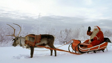 Weihnachtsmann auf seinem von einem Rentier gezogenen Schlitten im Schnee | Bild: picture-alliance/dpa